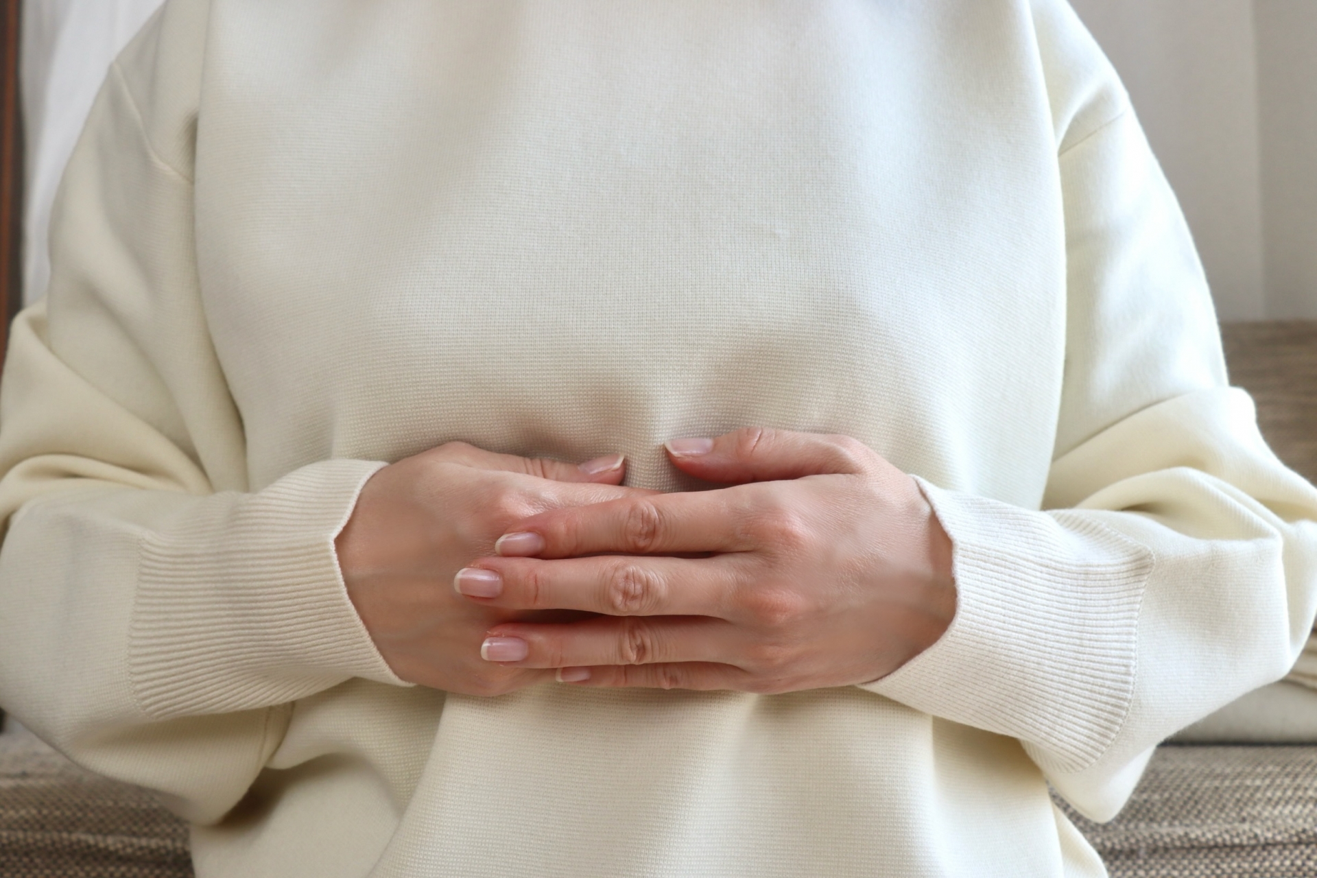 お腹の張りを気にしてソファで腹部に手を当てる女性