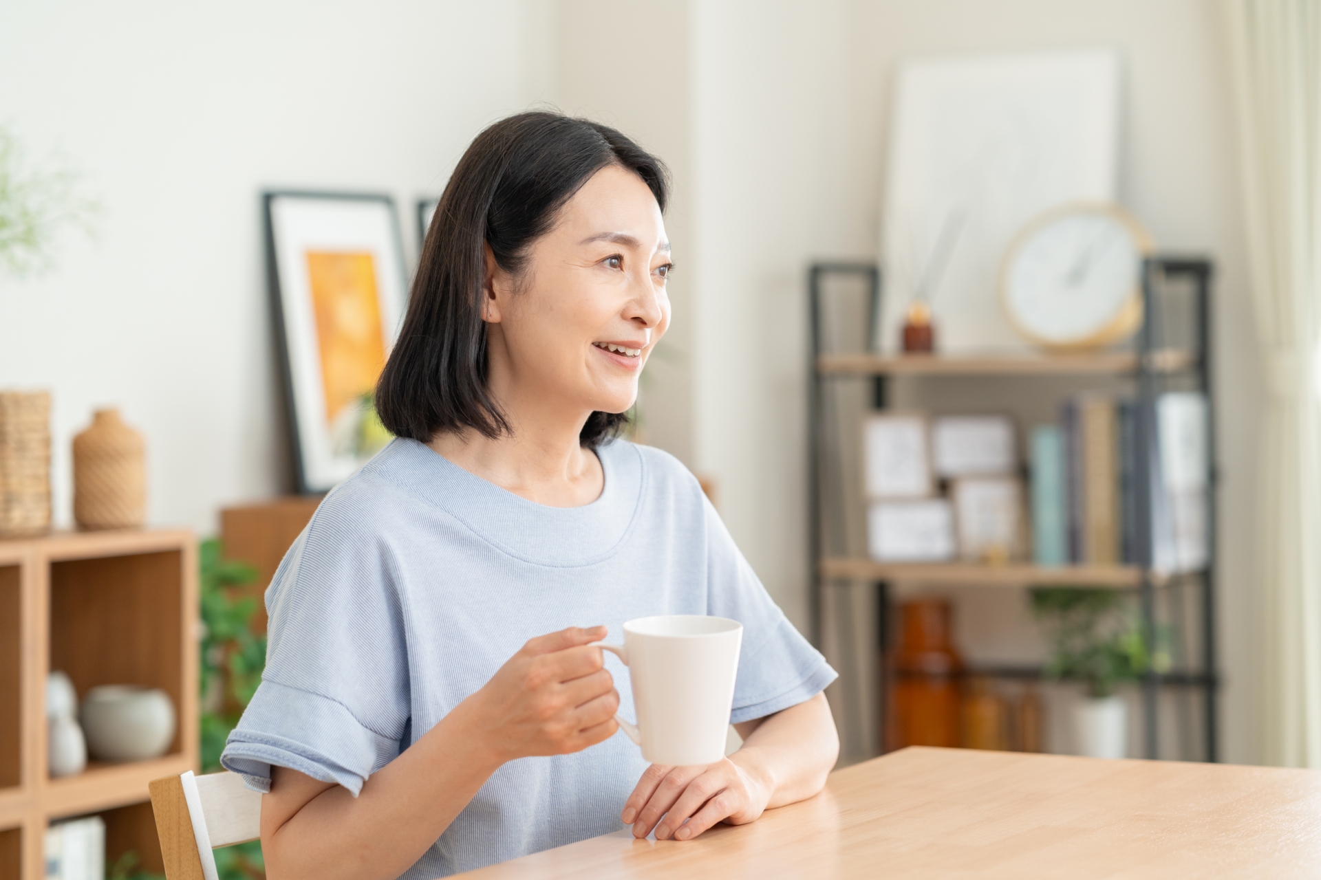 やさしい光の差し込む窓辺で温かい飲み物を手に深呼吸する30〜40代の女性