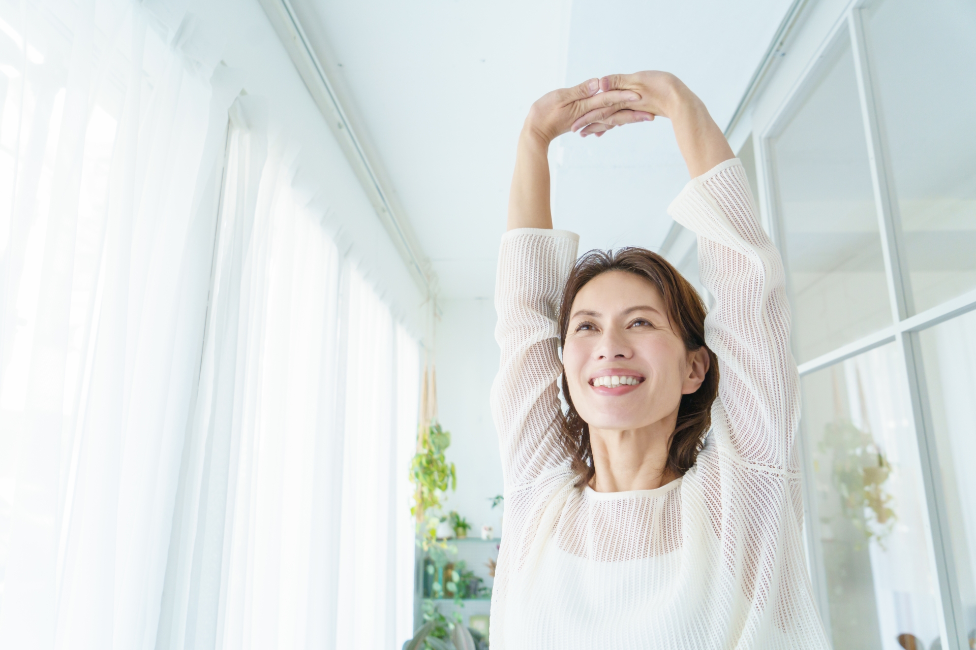 朝の光の中で伸びをしている健康的な女性の後ろ姿