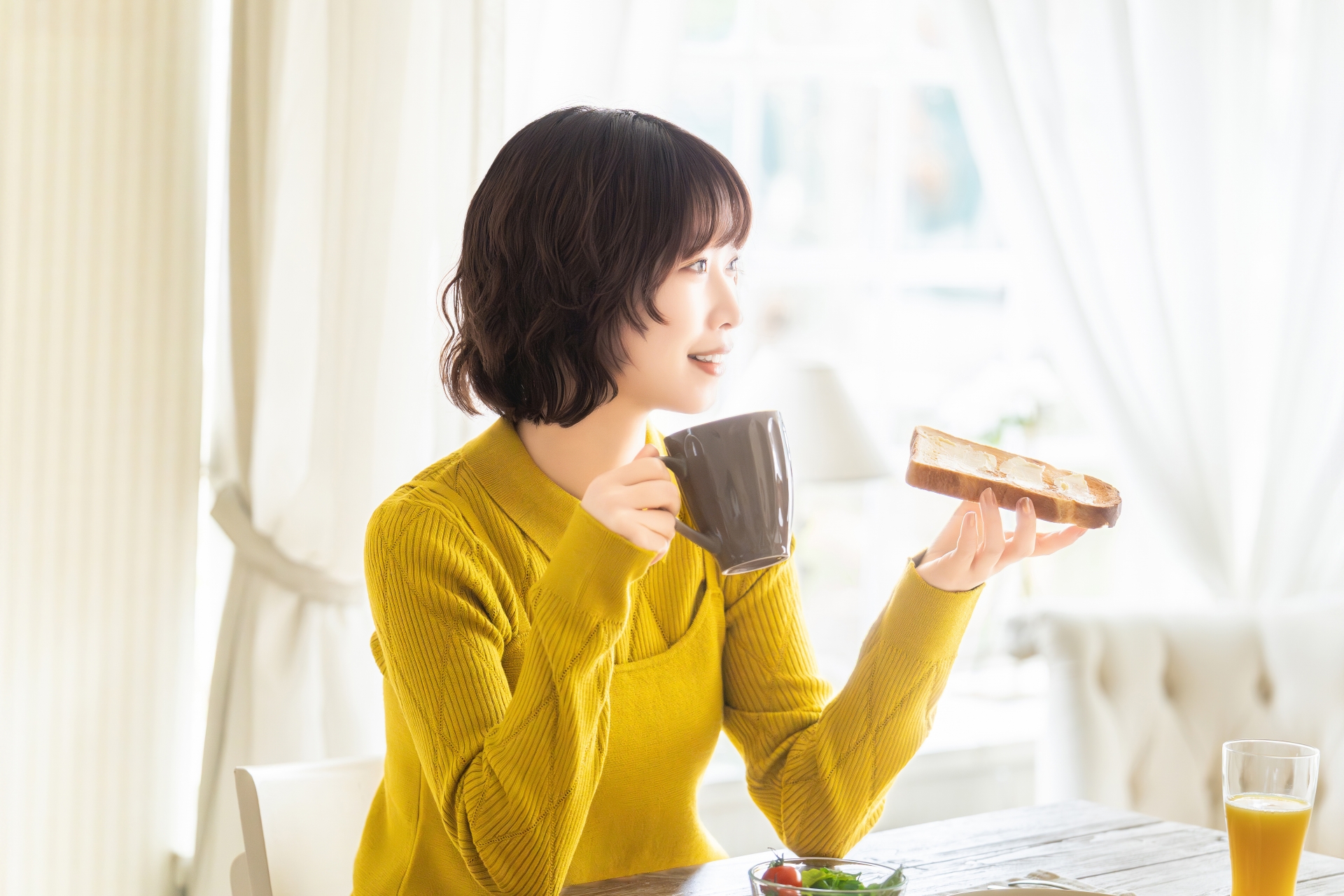 朝のダイニングテーブルでドリンクを手に取る女性