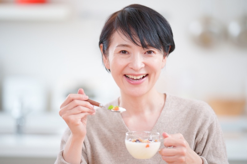 朝食のヨーグルトとサプリを手に取る女性