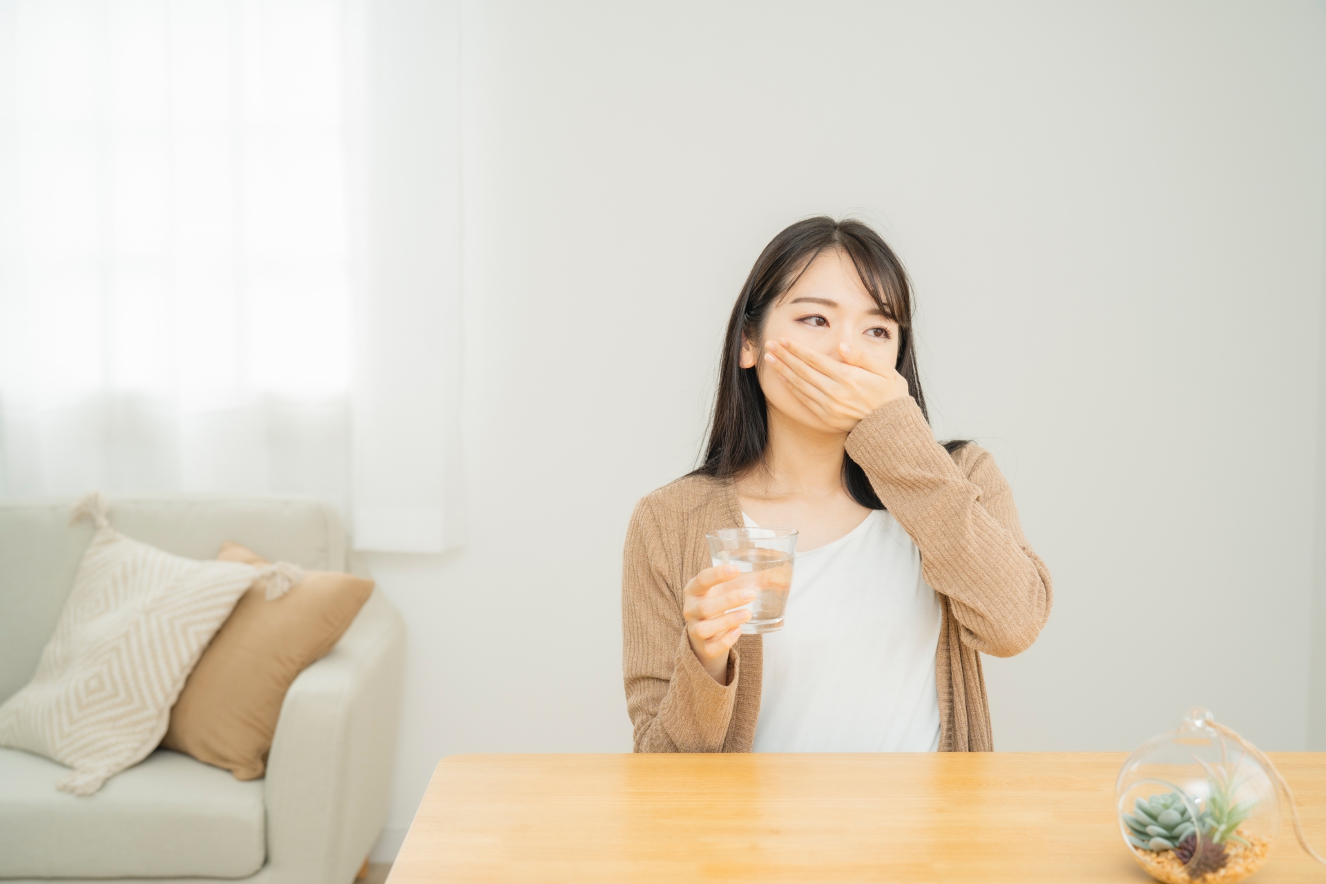 朝のテーブルでコップの水と一緒に整腸薬を飲もうとする女性の手元