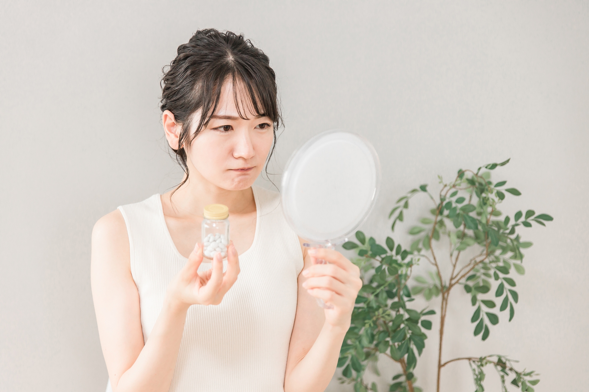サプリメントを手に持ちながら考えている女性