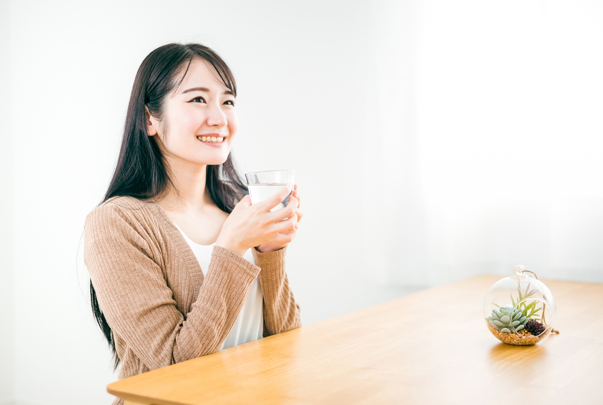 朝の食卓で温かい白湯の入ったコップを手にする女性