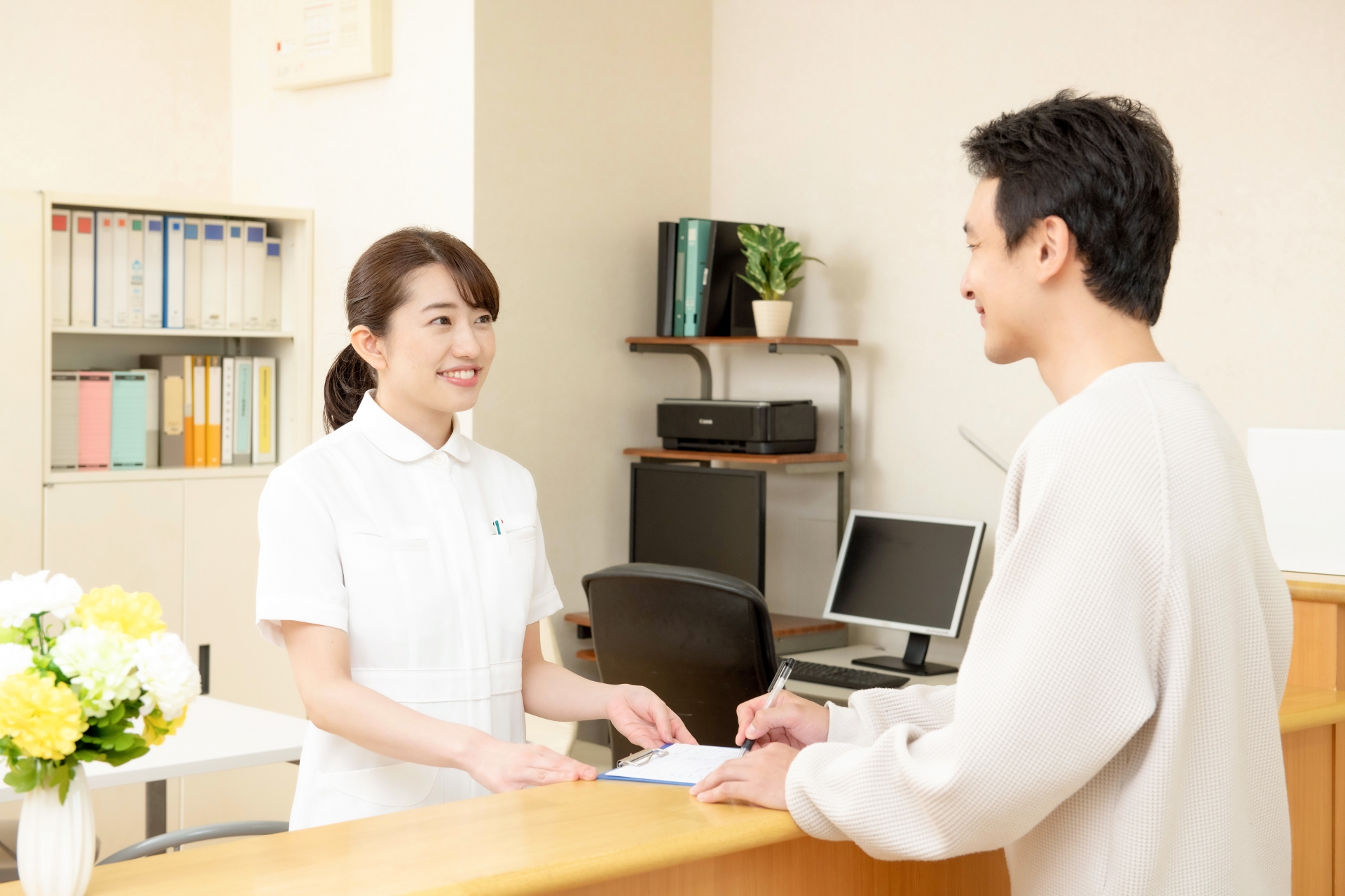 内科クリニックの受付窓口で問診票を記入する女性