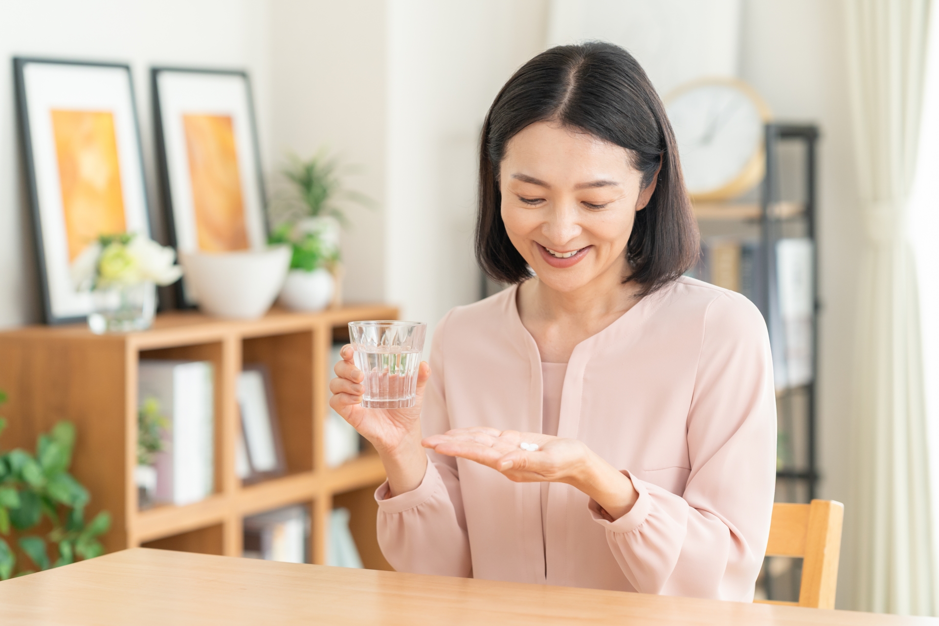 食後にサプリメントと水を手に取る女性の手元