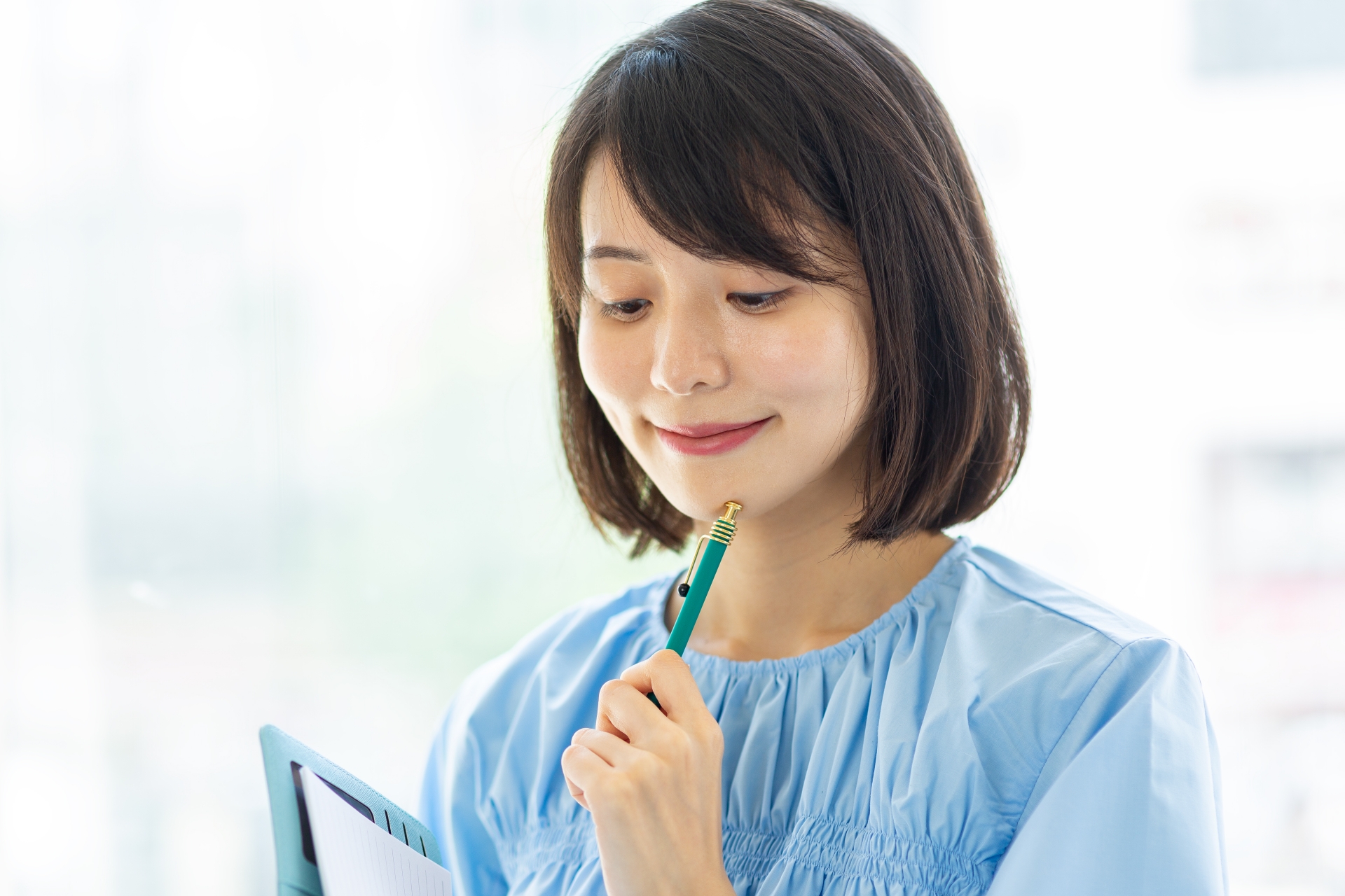 何かを考える表情でメモやスマホを手にする女性
