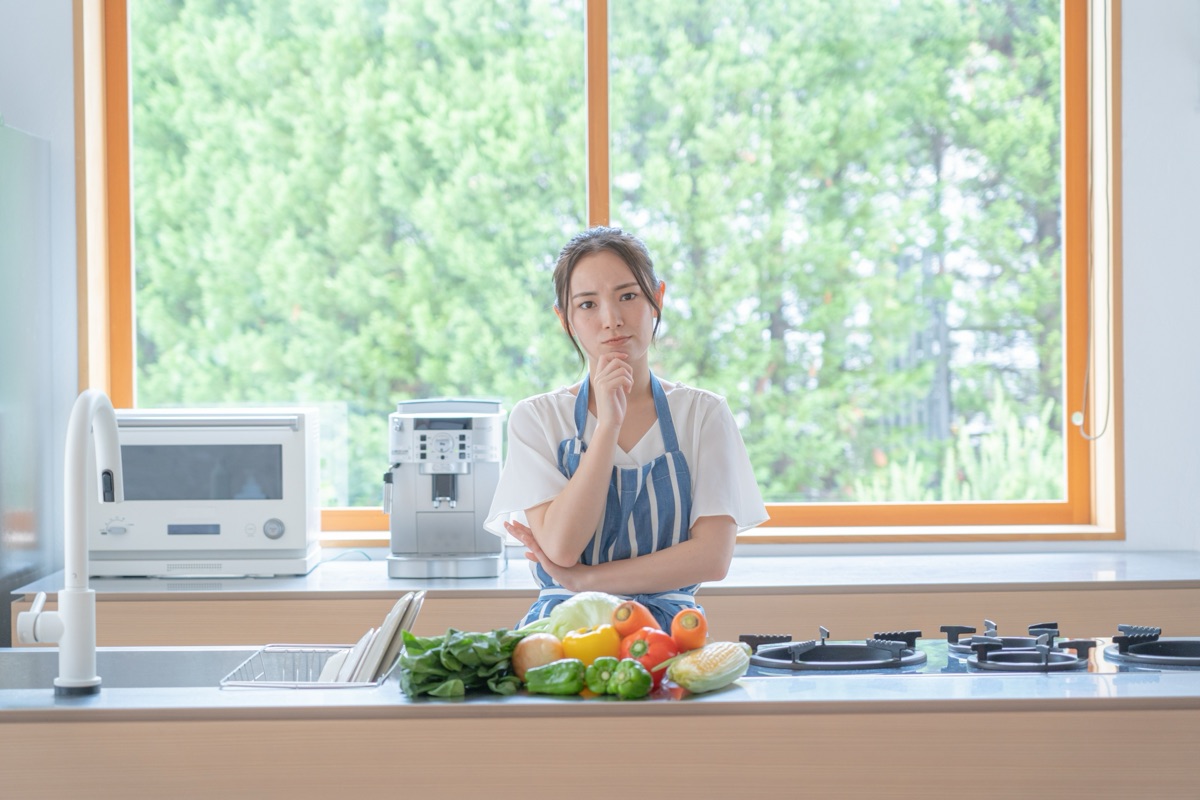 キッチンで何を食べればよいか考える女性のイメージ