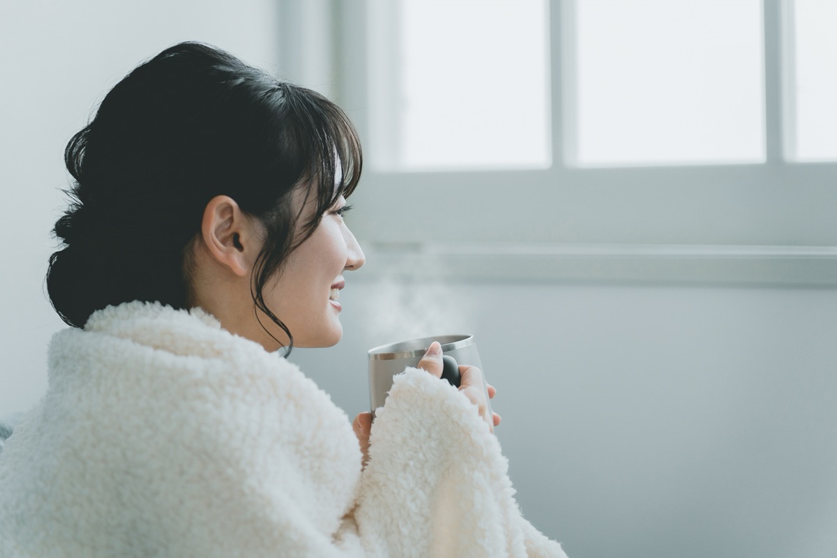 湯気の立つ白湯のマグカップを両手で持つ女性のイメージ