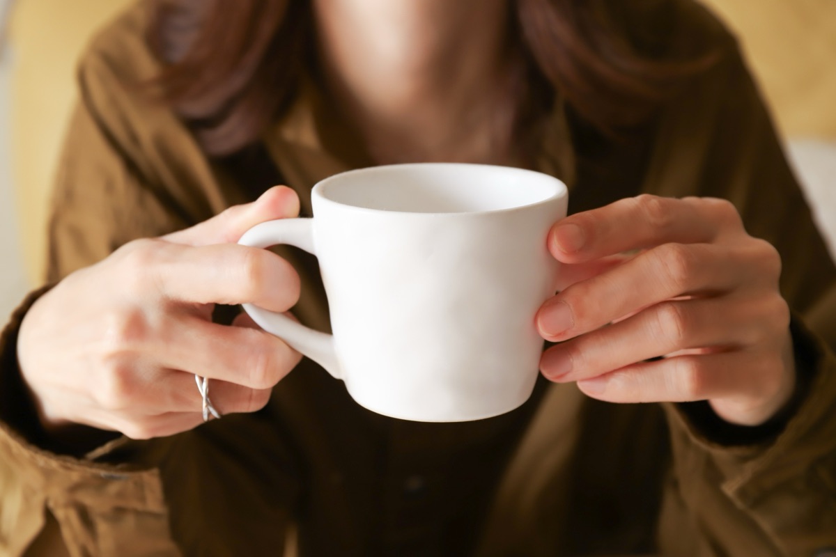 温かいカップを両手で包んで温もりを感じる女性のイメージ