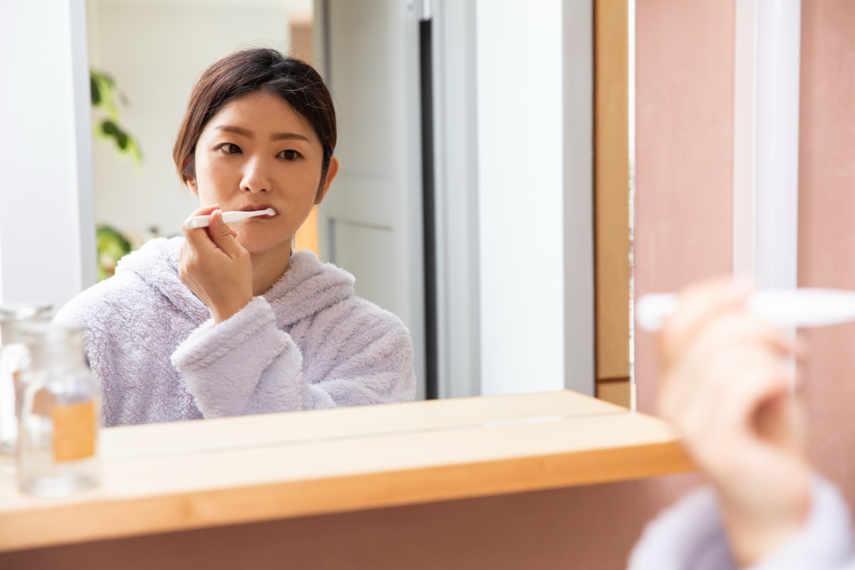 洗面所で舌ブラシによるオーラルケアをする女性のイメージ