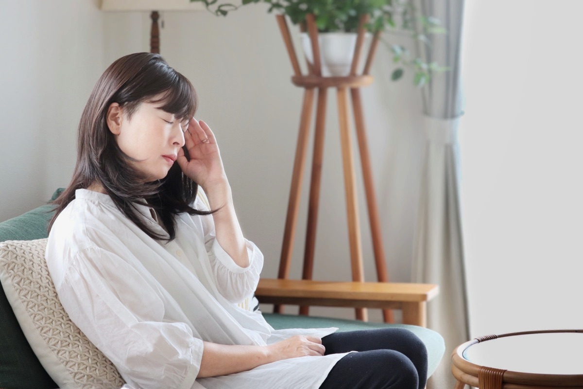 頭痛やふらつきを感じてこめかみを押さえる女性のイメージ