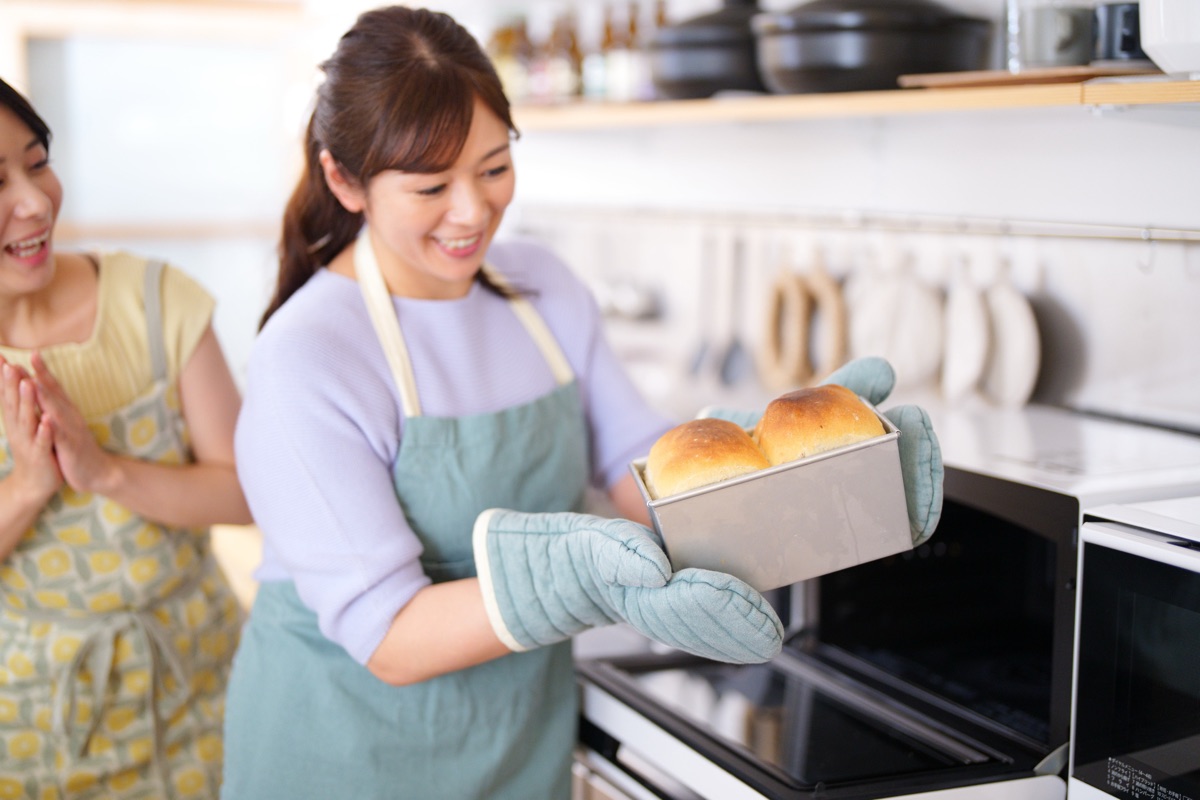 オーブンから焼き上がったパンを取り出す女性のイメージ