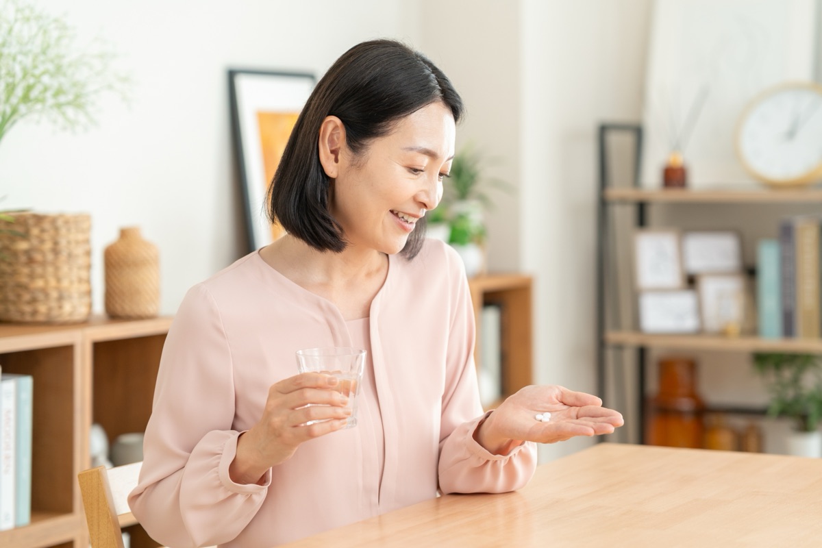 食後のダイニングテーブルで錠剤とコップの水を手に持っている女性の手元