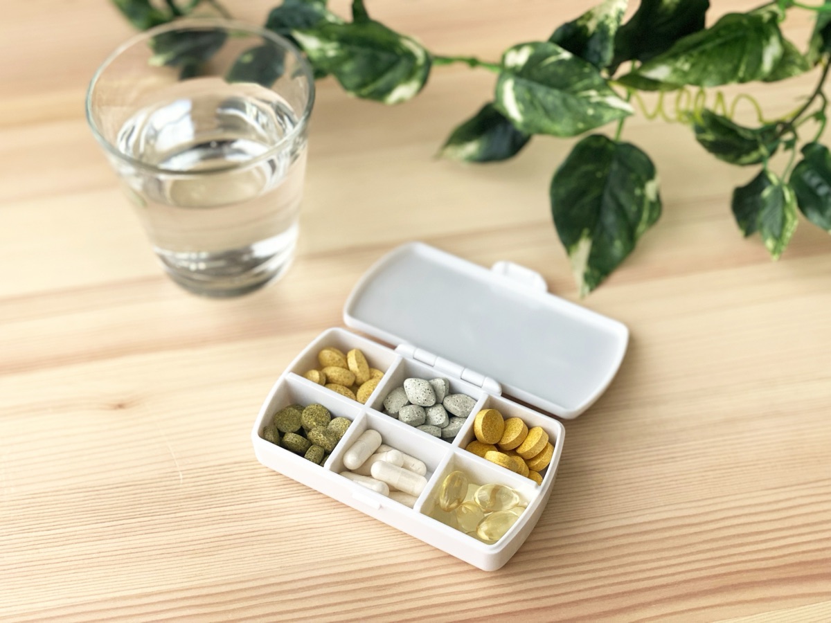 朝の食卓でサプリと水を手に取る女性のイメージ