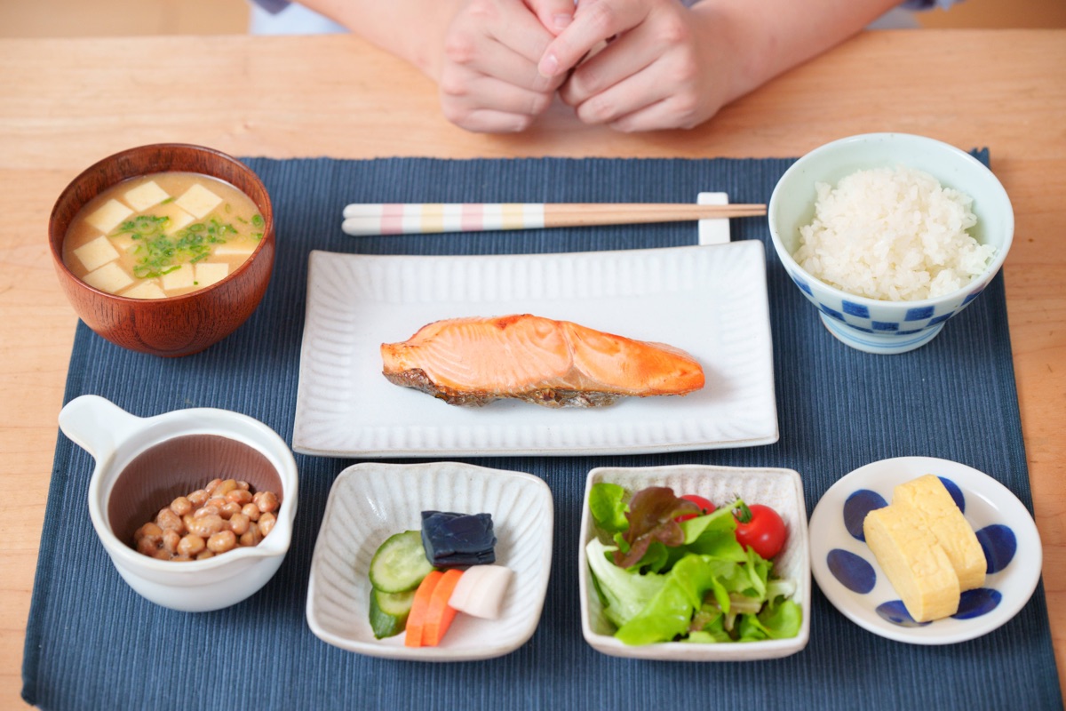朝の食卓でぬか漬けとサプリメントを手に取り、毎日の習慣として続ける様子のイメージ